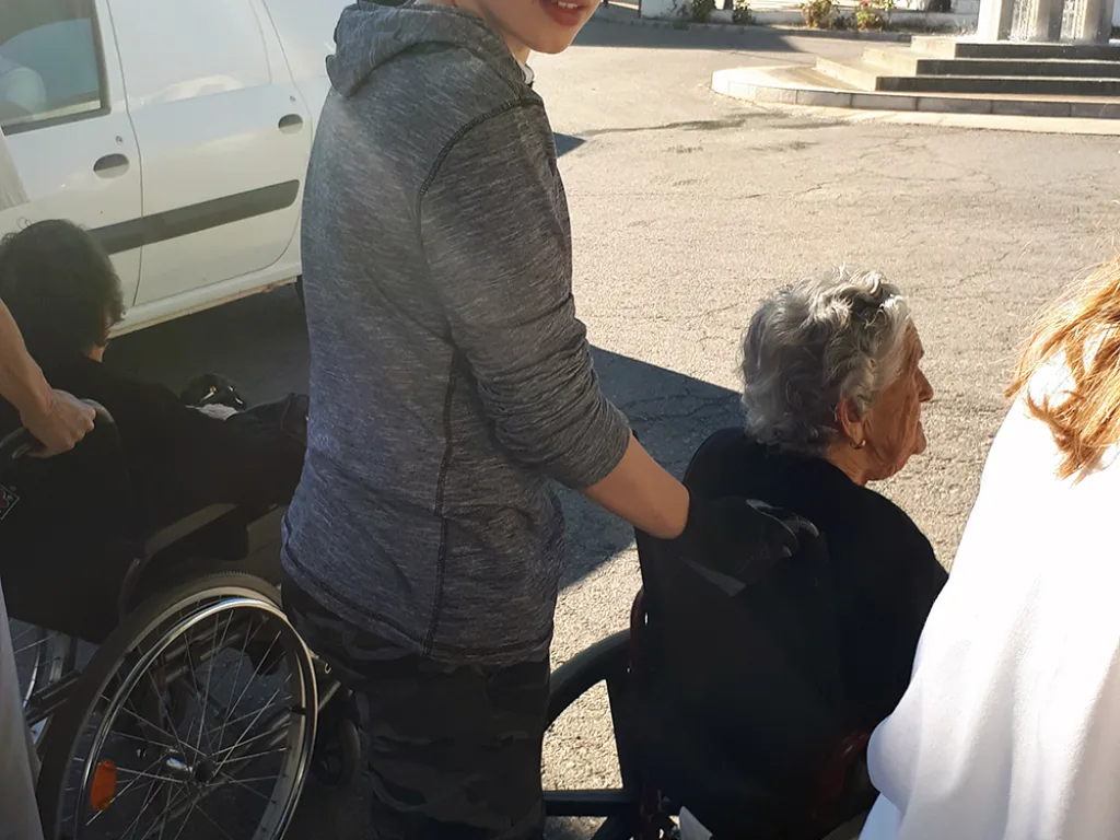 Ein Jugendlicher hilft einer älteren Person im Rollstuhl.